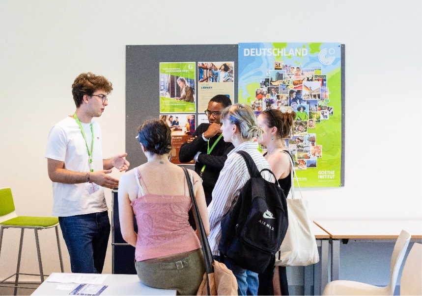 Five students standing and talking in front of German posters.