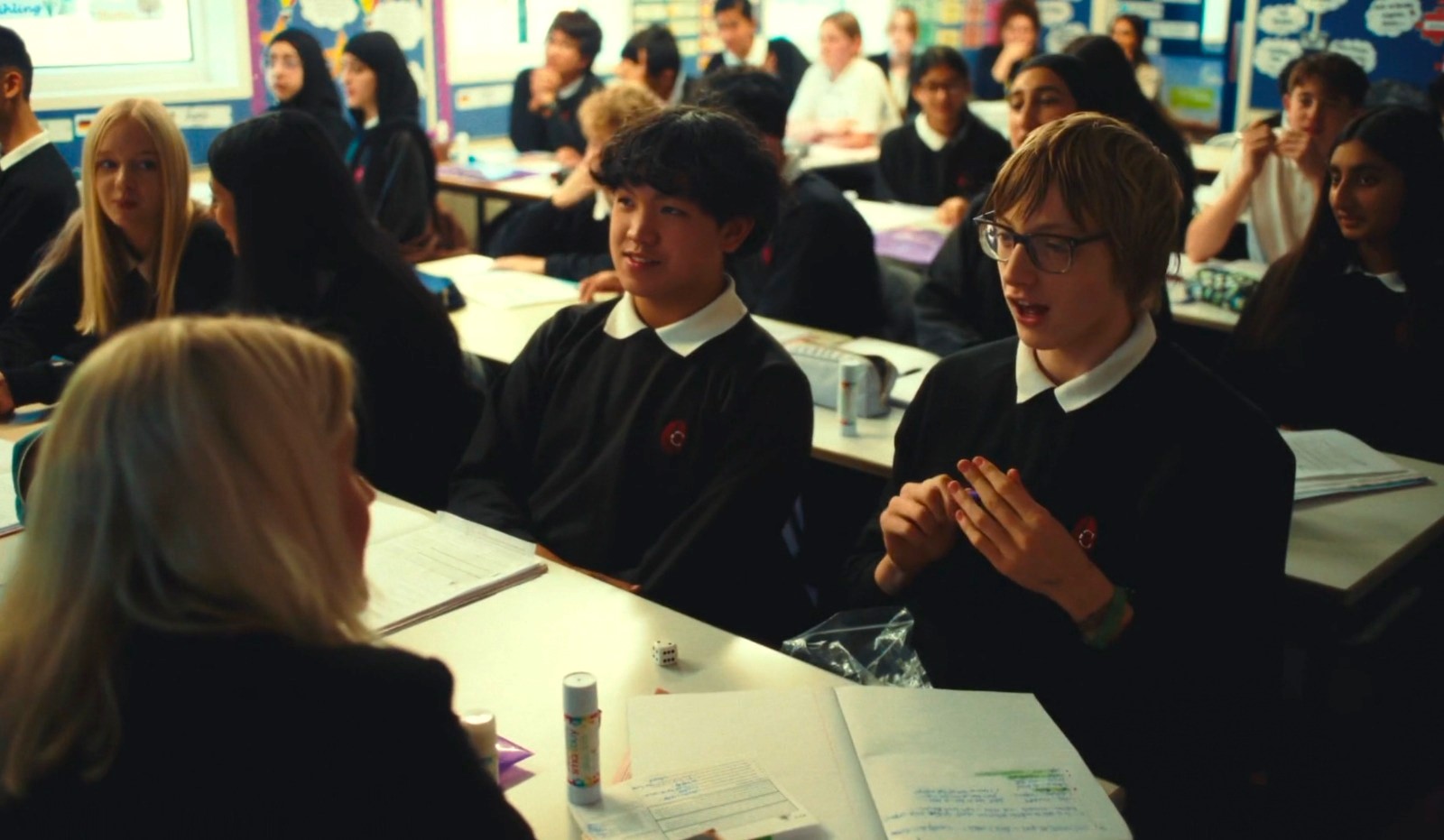 A photo of a teacher speaking with two pupils at their desk