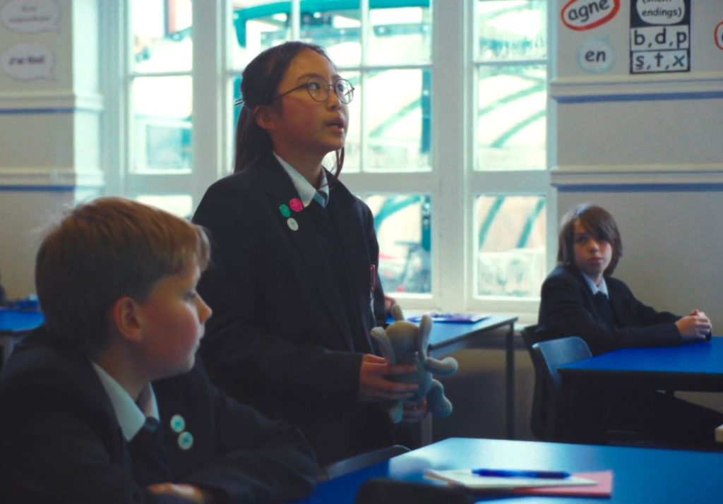 A photo of a pupil talking and holding a teddy during a speaking activity